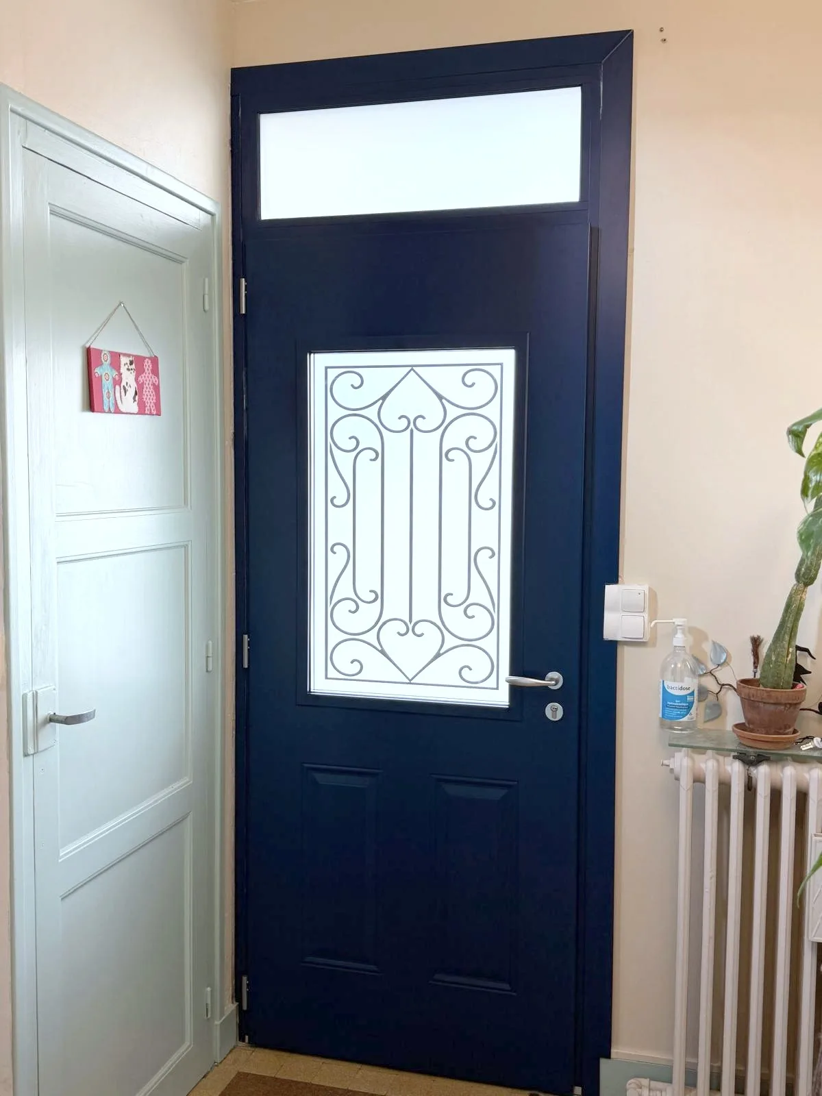 La même porte bleu marine vue de l'intérieur de l'entrée, vitrage dépoli à motif de ferronnerie et poignée inox