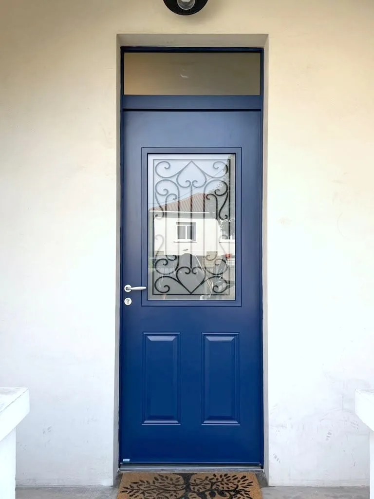 Porte d'entrée bleu marine posée sous imposte vitrée, vue de l'extérieur : vitrage décoré de ferronnerie noire et deux panneaux moulurés